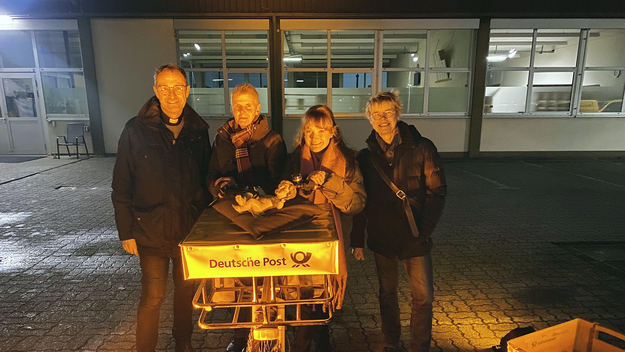 Pfarrer Jörg Meyrer, Ulrike Phiesel, Nadine Kreuser und Bärbel Knieps vom Vor­bereitungsteam mit der Figur des Jesuskinds, das von einem Postboten per Fahrrad geliefert wurde.